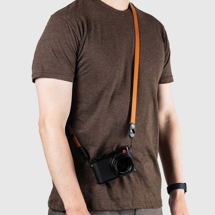 Person wearing a brown t-shirt with a camera attached to an Amber Form Leather Strap Long on a plain background
