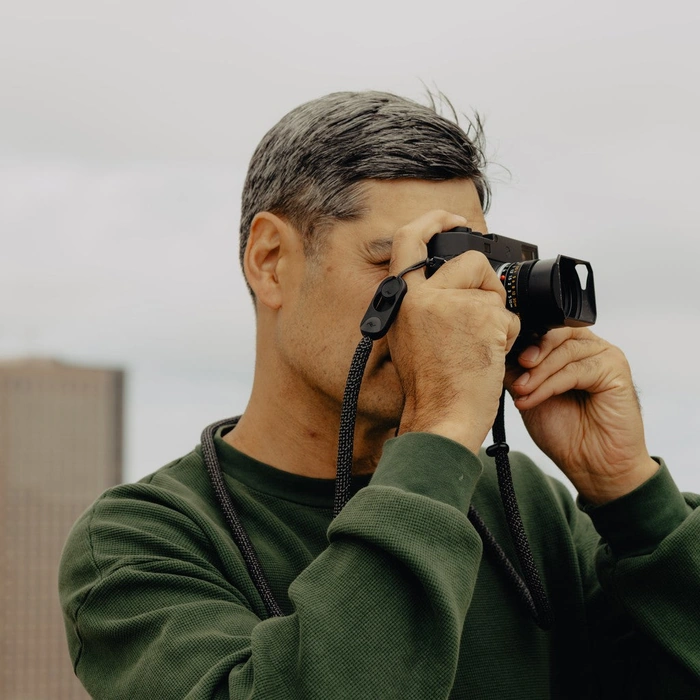 Man taking a photo with a camera attached to Long Black Form Rope Strap against a neutral background