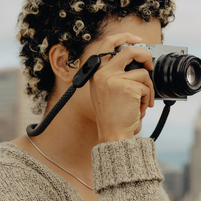 Person holding a camera attached to Black Rope Strap