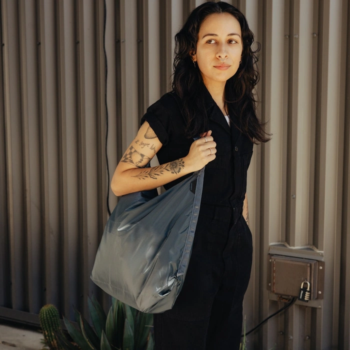 Woman holding a Packable tote Ocean against a metallic wall.