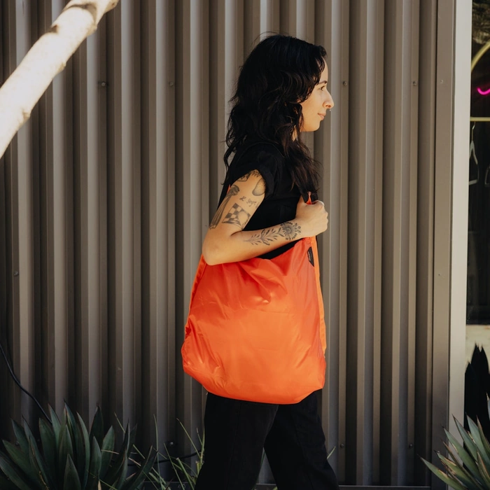 Person holding an Packable tote Ibis against a corrugated metal wall.