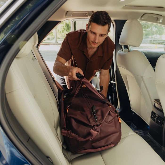 Man loading a Travel Duffel 35L Eclipse into the back seat of a car.