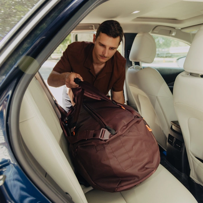 Man loading a 65L Eclipse Travel Duffel into the back of a car